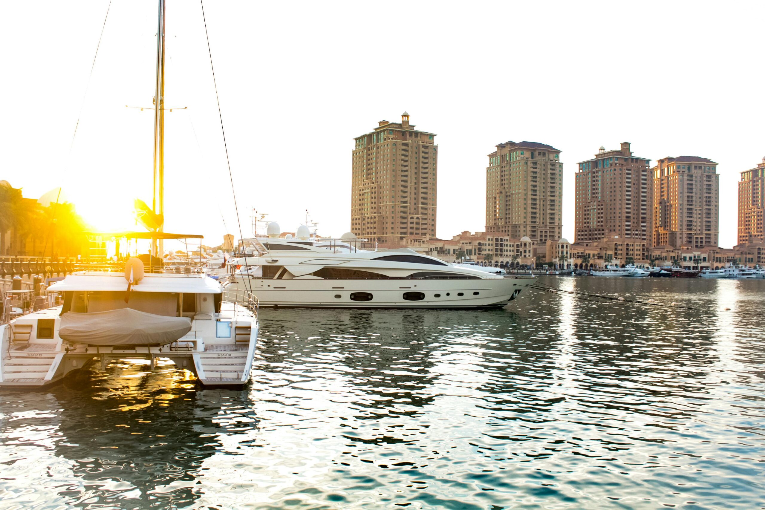 Scenic view of yachts docked at Doha marina with striking skyscrapers at sunset.