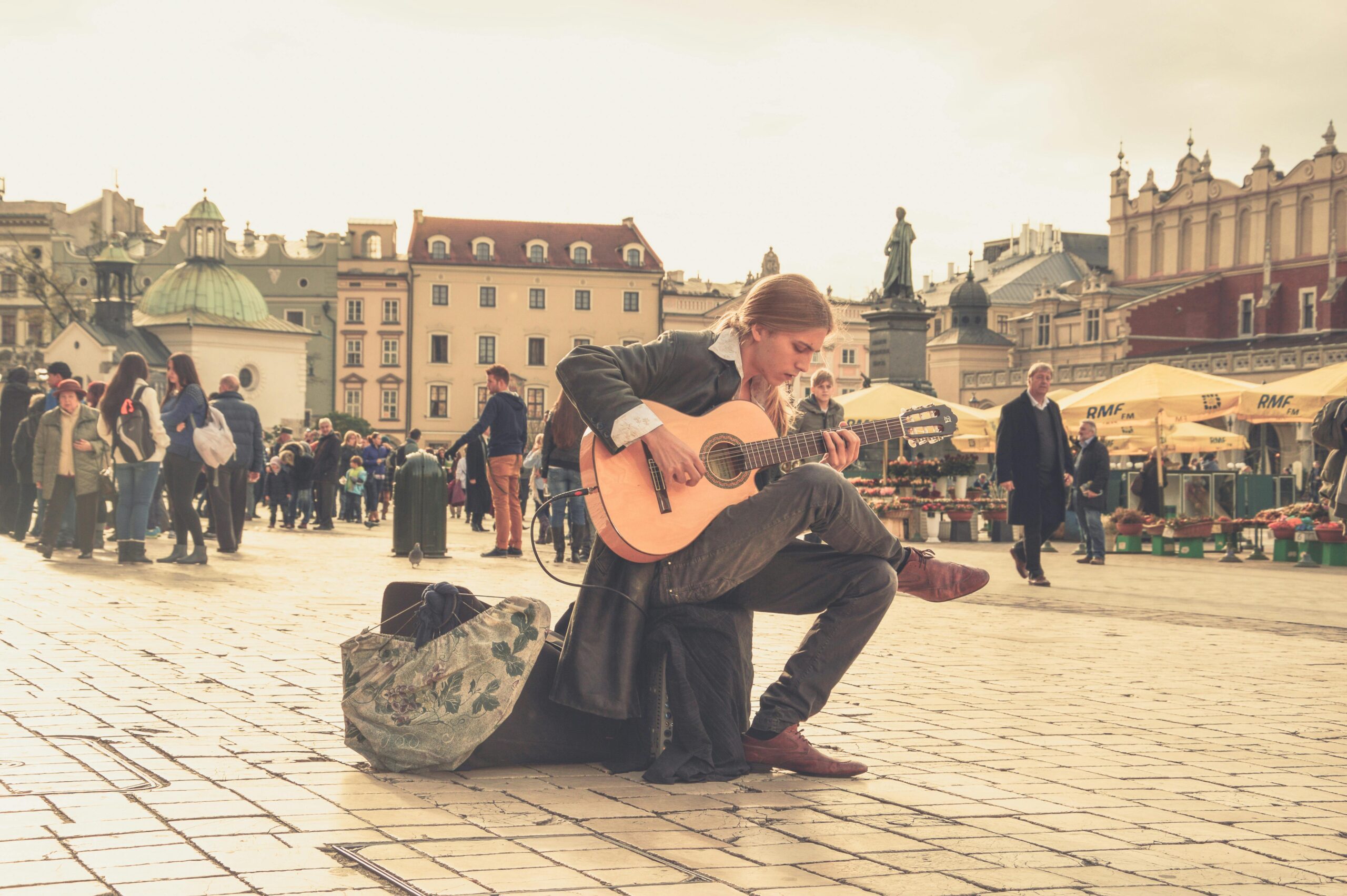 A street performer playing guitar in a vibrant old town square with a lively crowd.