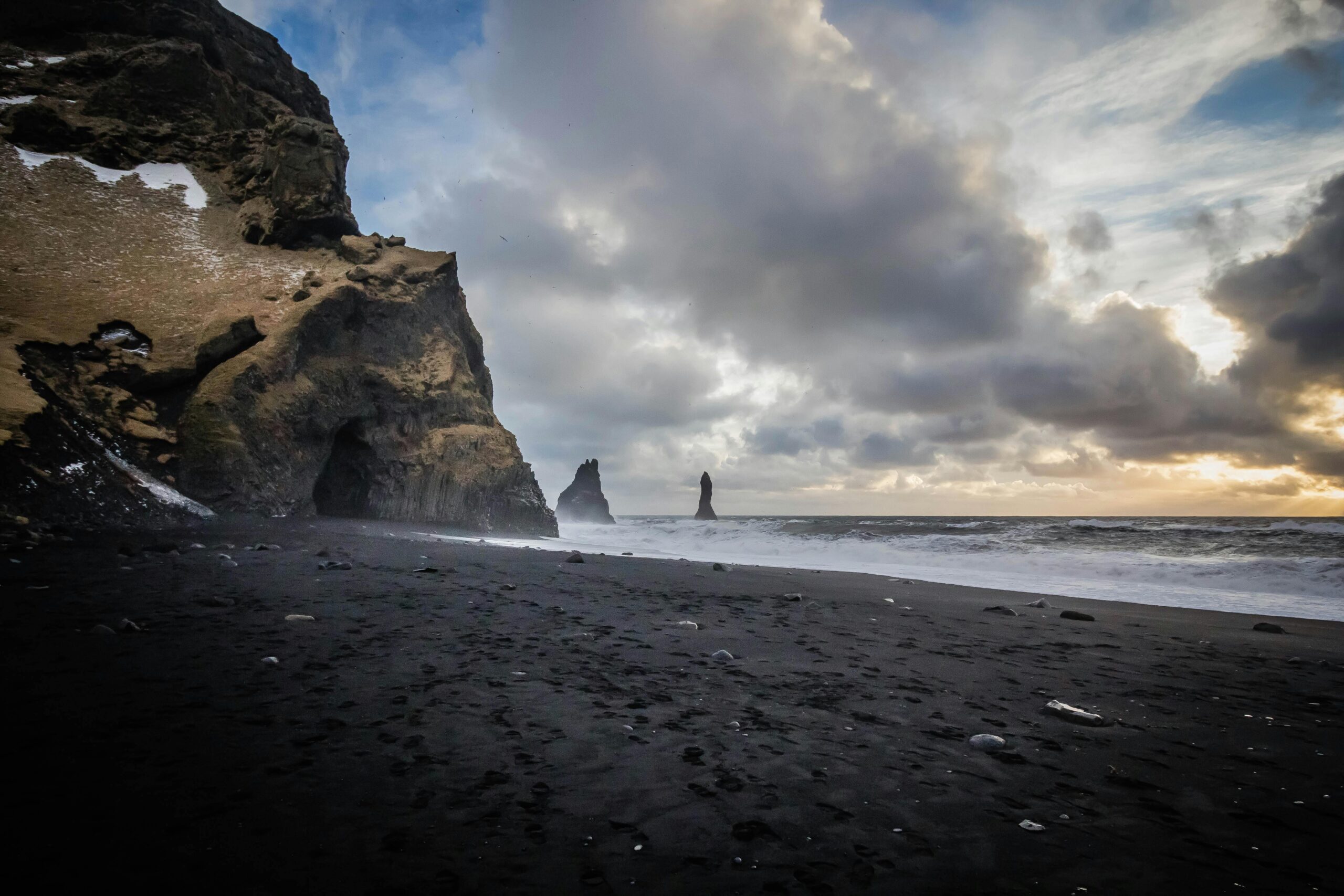 Stunning view of Reyniskirkja beach with black sand, cliffs, and ocean waves in Vík, Iceland.