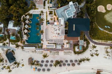 Aerial shot of a luxurious beachfront resort in Playa del Carmen, showcasing pools, loungers, and the sandy beach.