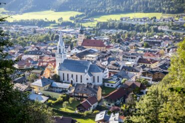 Stunning aerial view of a picturesque Alpine village nestled in lush surroundings featuring a prominent church.