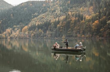 A group enjoys a peaceful fishing trip on an Austrian lake surrounded by beautiful autumn foliage.