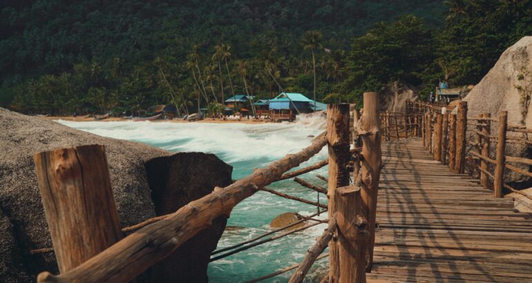 Rustic wooden pier with lush coconut trees and vibrant blue ocean waves on a tropical island beach.