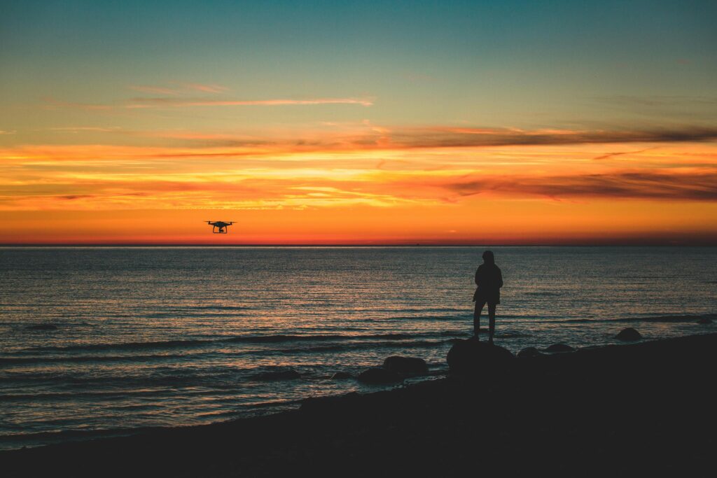 Captivating sunset with a drone flying over the Baltic Sea, featuring a silhouetted person on the shore.