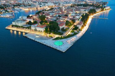 Stunning aerial shot of Zadar's coastal cityscape at dusk, with landmarks and waterfront brightly illuminated.
