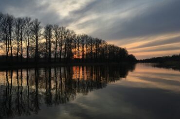 Tranquil sunset over a lake with bare trees reflected on the water in Tartu, Estonia.