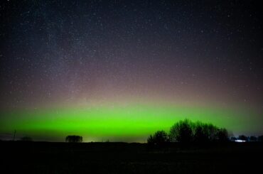 Captivating view of the aurora borealis illuminating a starry night sky over rural Lithuania.