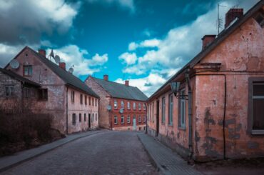 Historic street with old houses in Kuldīga, Latvia, showcasing classic architecture under a blue sky.