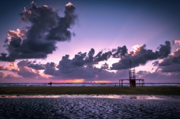 Dramatic sunset at Chania beach with clouds and a lone figure silhouetted against the sky.