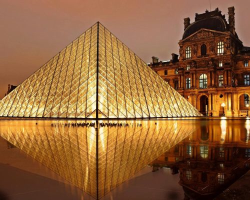 Stunning nighttime view of the illuminated Louvre Pyramid and reflection in Paris, France.