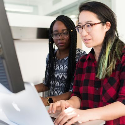 Two women working on a computer project together in an office setting.