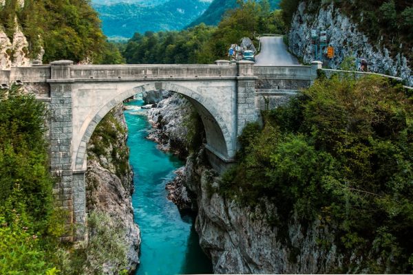 Scenic view of a stone arch bridge over a vibrant turquoise river framed by lush greenery.