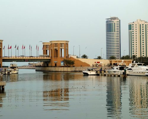 A modern marina with yachts, bridge, and waterfront city skyline reflecting on calm waters.