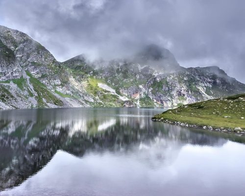 Scenic view of a tranquil lake surrounded by misty mountains in the Rila Mountains, Bulgaria.