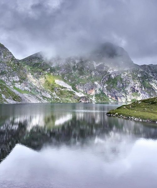 Scenic view of a tranquil lake surrounded by misty mountains in the Rila Mountains, Bulgaria.