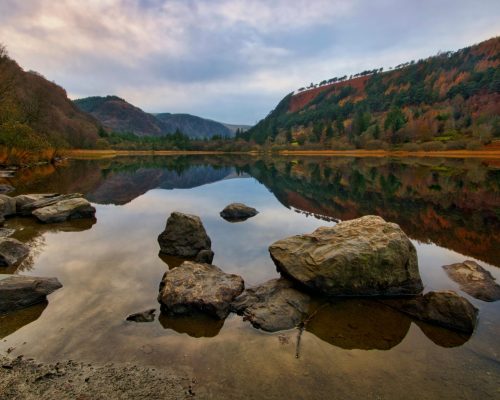 A serene early morning view at Glendalough Lake, Ireland, with stunning autumn foliage reflected in calm waters.