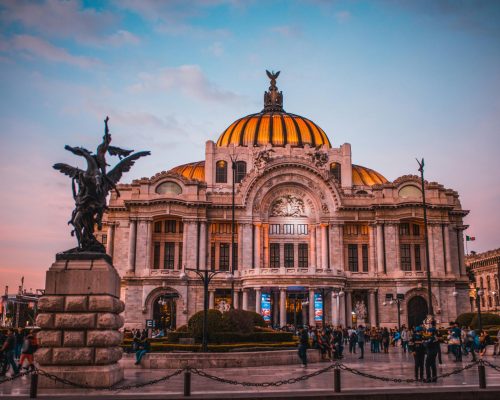 Vibrant sunset at the historic Palacio de Bellas Artes in Mexico City, bustling with tourists.
