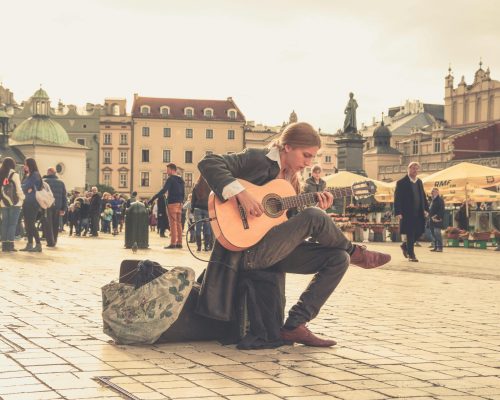 A street performer playing guitar in a vibrant old town square with a lively crowd.