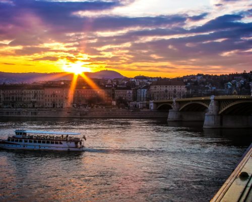 Scenic sunset over Budapest featuring the iconic Margaret Bridge and river cruise boat.