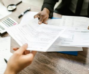 Two professionals exchanging documents in an office setting, focusing on paperwork and data analysis.