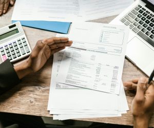 Hands holding financial documents with calculator and laptop on office desk, business analysis scene.