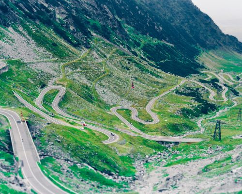 Aerial view of the winding Transfagarasan Highway in the Romanian mountains, showcasing lush greenery.
