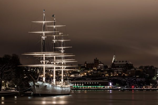 A majestic illuminated sailboat moored in Stockholm's harbor at night, showcasing beautiful city lights.